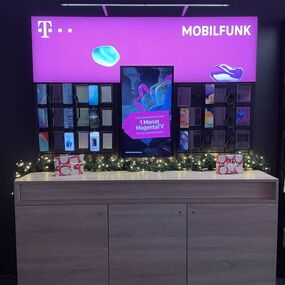 Telekom Mobilfunk Shop mit beleuchteter Auslage, Smartphones und festlicher Dekoration.